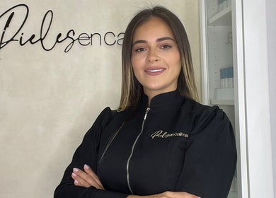 Especialista de Pieles en Calma en Gurabo, PR, sonriendo frente a la pared con el logotipo del centro.