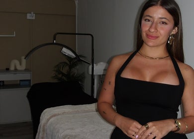 Esteticista en Skin Diary, Toa Baja, PR, junto a una cama de tratamiento en elegante sala de belleza.