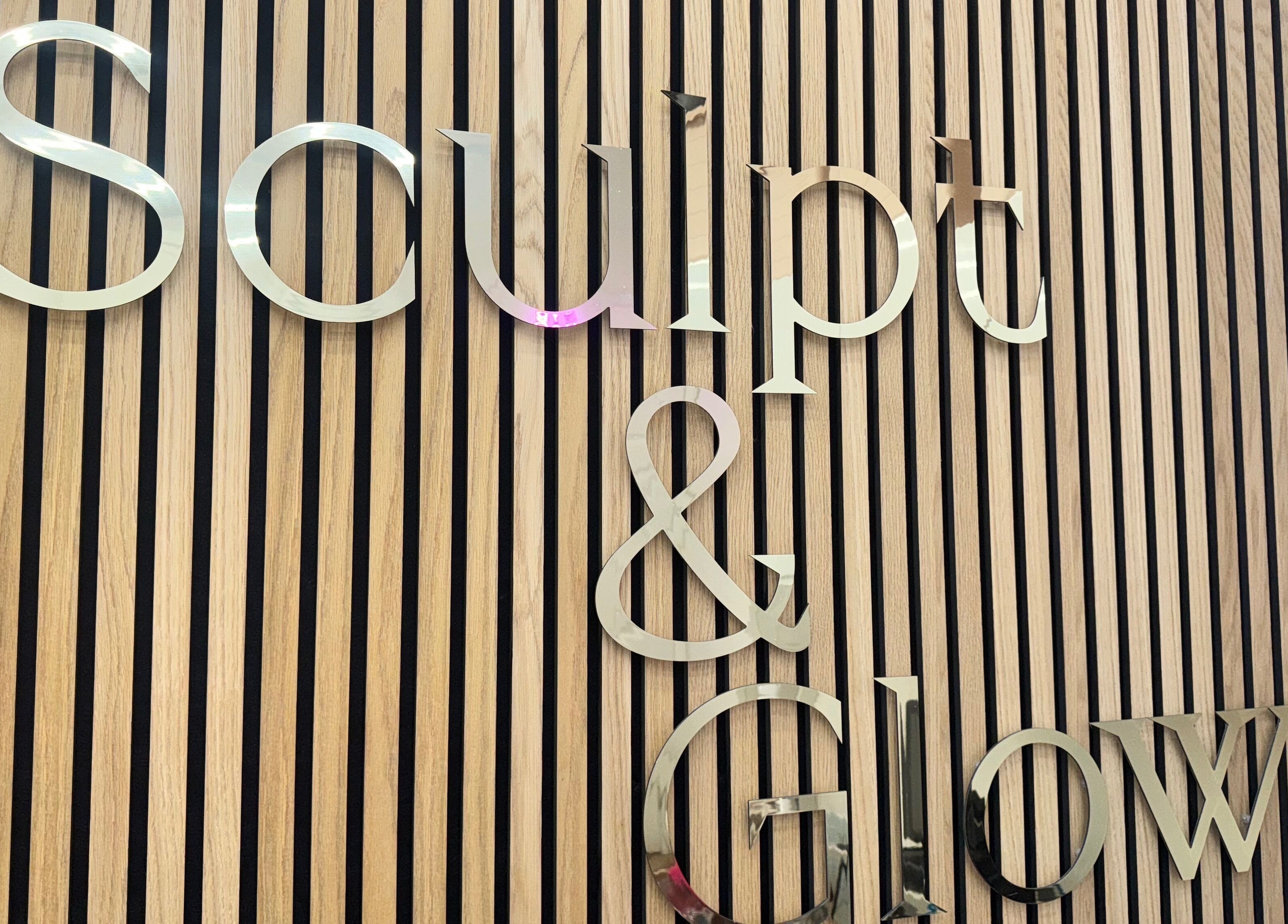 Stylish metal sign of Sculpt and Glow by Katrina at Brentwood, England, GB on wooden slatted wall.