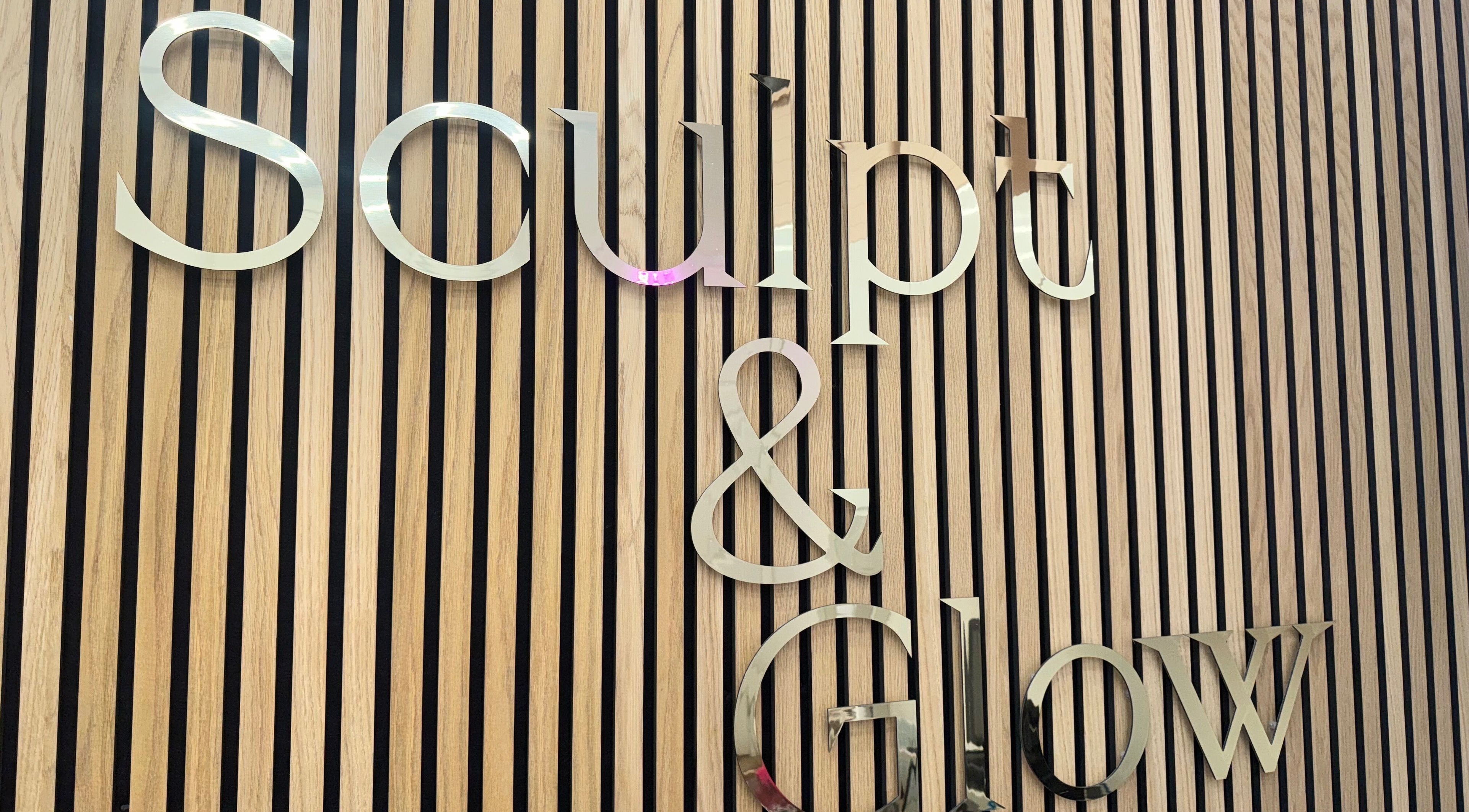 Stylish metal sign of Sculpt and Glow by Katrina at Brentwood, England, GB on wooden slatted wall.