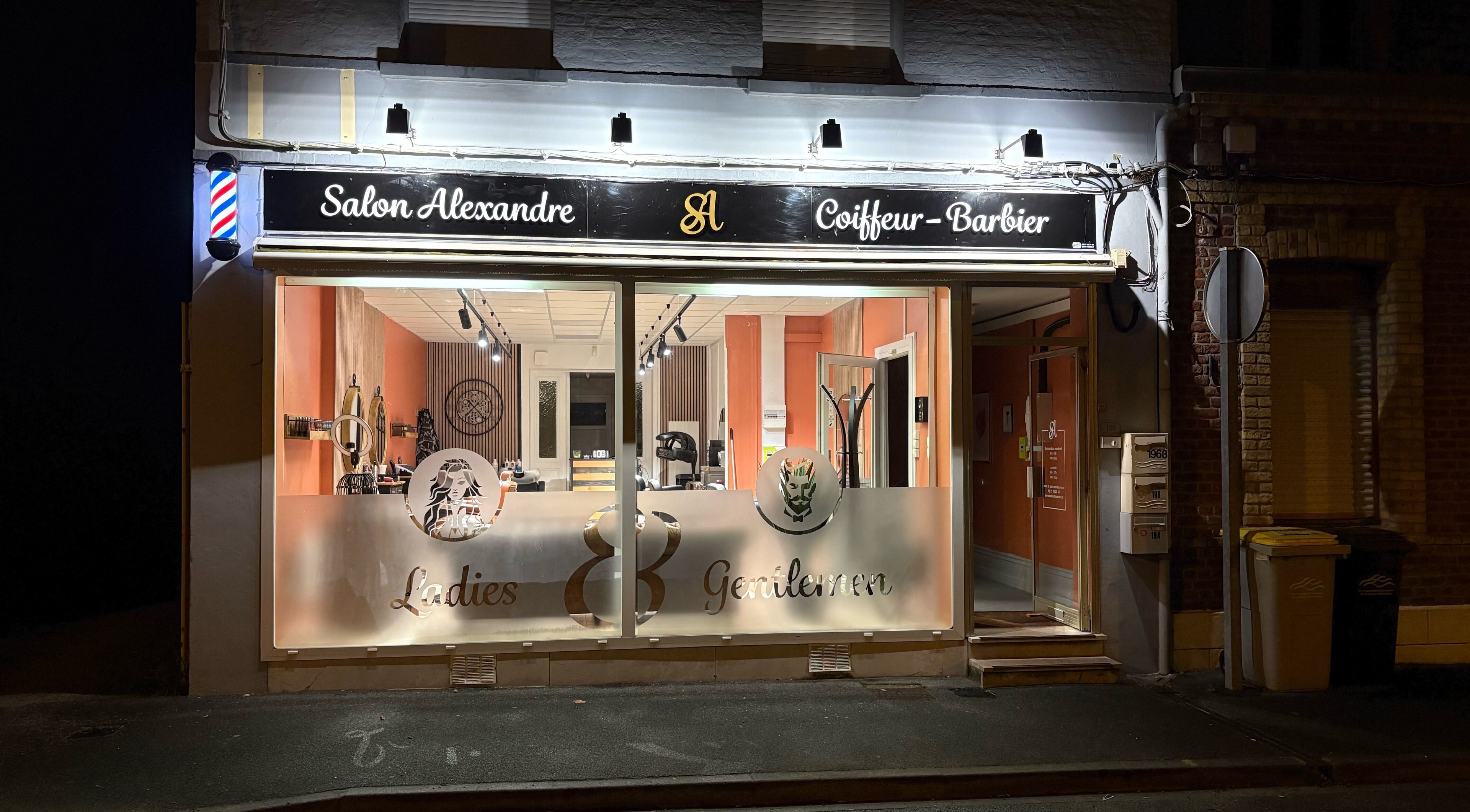 Façade de Salon Alexandre à Audruicq, Hauts-de-France, FR, éclairée la nuit, affichant le logo et la devanture.
