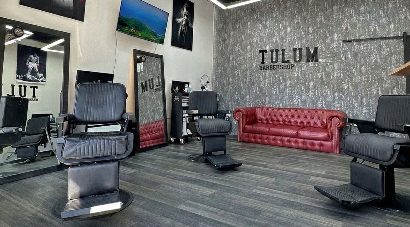 Interior elegante de Tulum Barbershop Barbería CDMX en Ciudad De México, MX con sillas de barbería y sofá rojo.