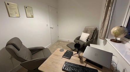 Cozy therapy room at Emily Bentham Hypnotherapy, Leicestershire, England, GB with comfortable chairs and a desk.
