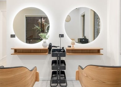 Modern styling station at Yasu's Salon, Melbourne, Victoria, AU, with round mirrors and sleek wooden chairs.