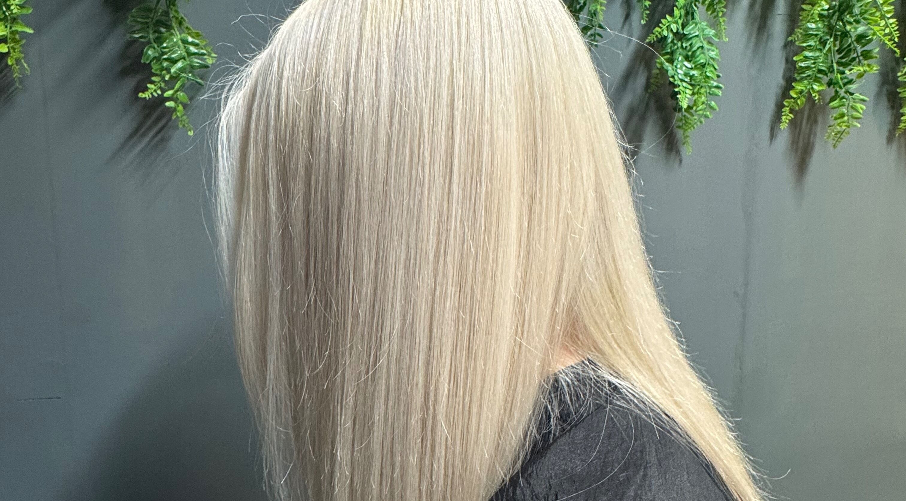 Sleek blonde hairstyle at Cherry On Top - Hair By Tom, Douglas, Douglas, IM with lush greenery backdrop.