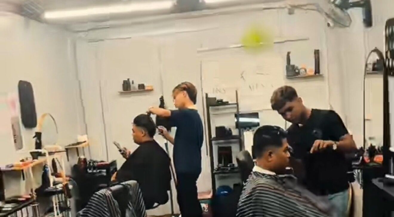 Inside Inspire Men's Barbershop, Kuala Lumpur. Two barbers styling hair with precise attention in a modern setting.