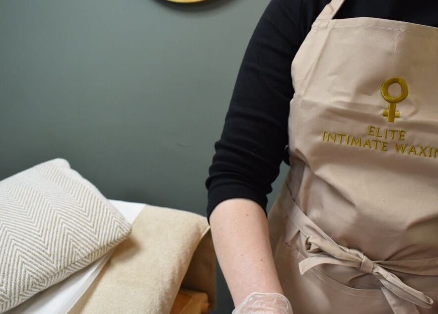 Staff in branded apron at Elite Intimate Waxing, Ruddington, England, GB, prepped for intimate waxing procedure.