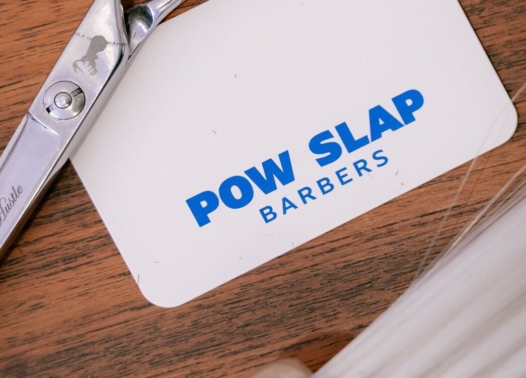 Close-up of Pow Slap Barbers card and silver scissors in Knutsford, England, GB.
