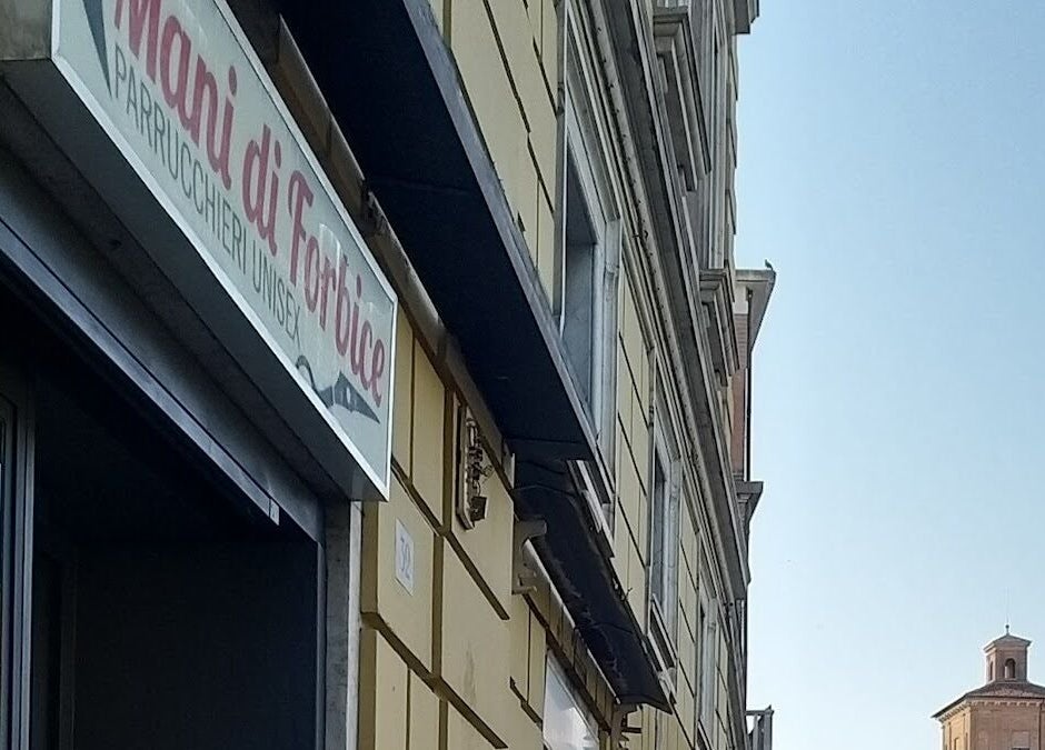 Insegna del salone Mani di Forbice a Ferrara, Emilia-romagna, IT con uno sfondo architettonico.