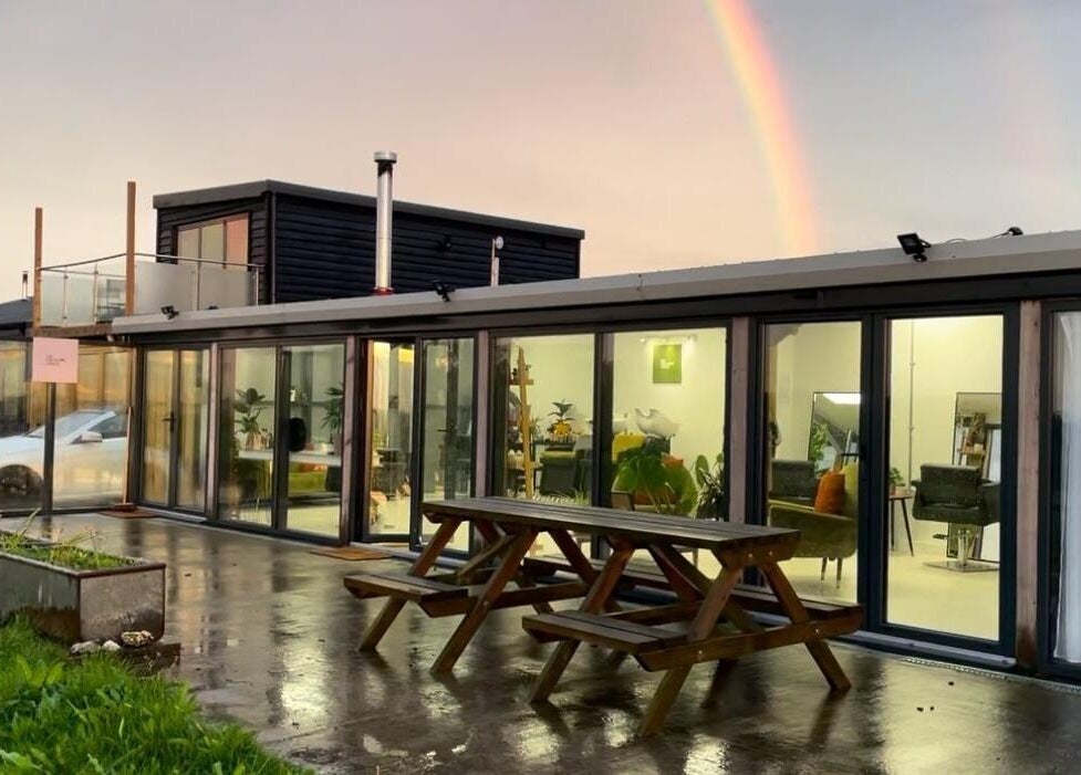 Joshua Rose Hair- Creative Space Kent in Faversham, England, with a rainbow over sleek glass exterior tables.