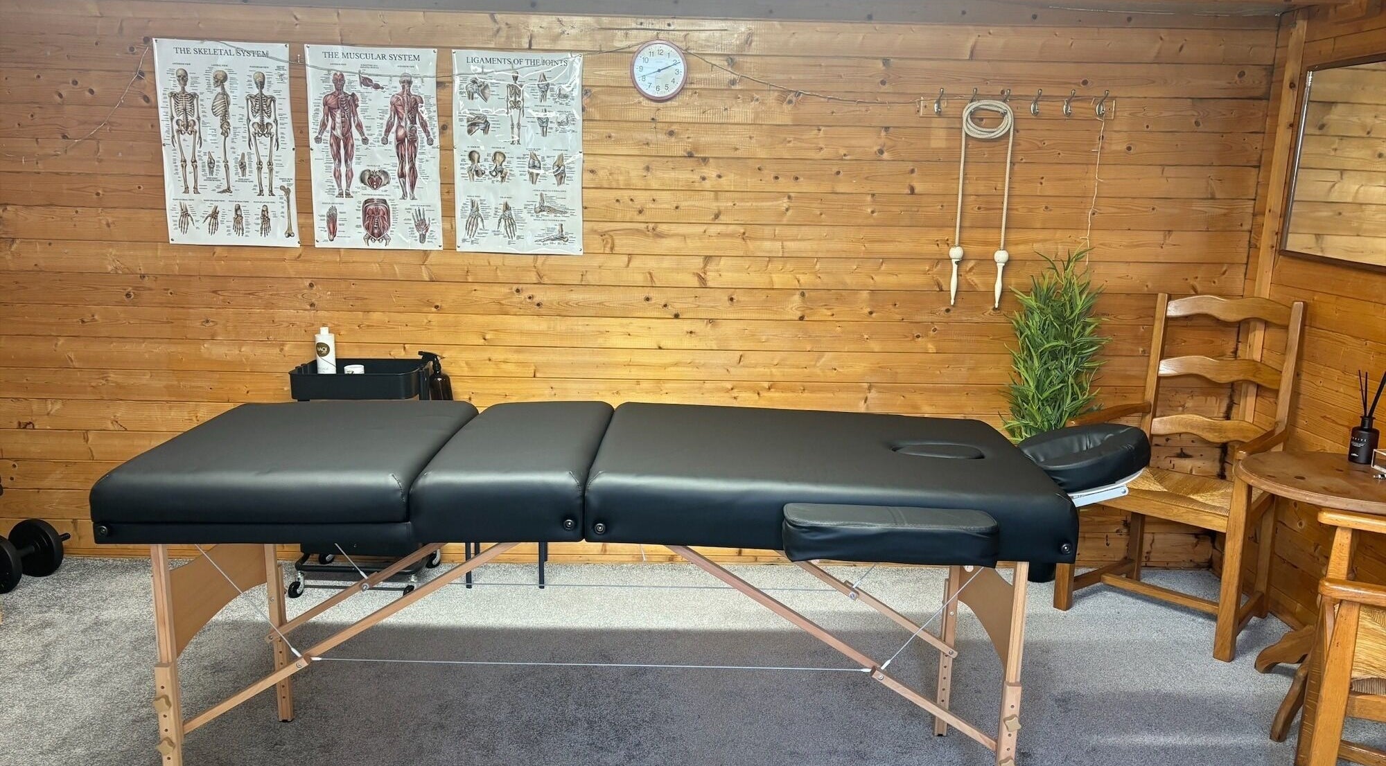 Therapy room at One Body - Private Healthcare Clinic, Langenhoe, England, GB with massage table and anatomical posters.