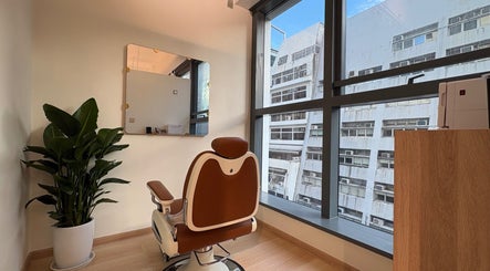 Luxurious barber chair at KOS Hair Salon, Hong Kong Island, HK, near a large window and indoor plant.