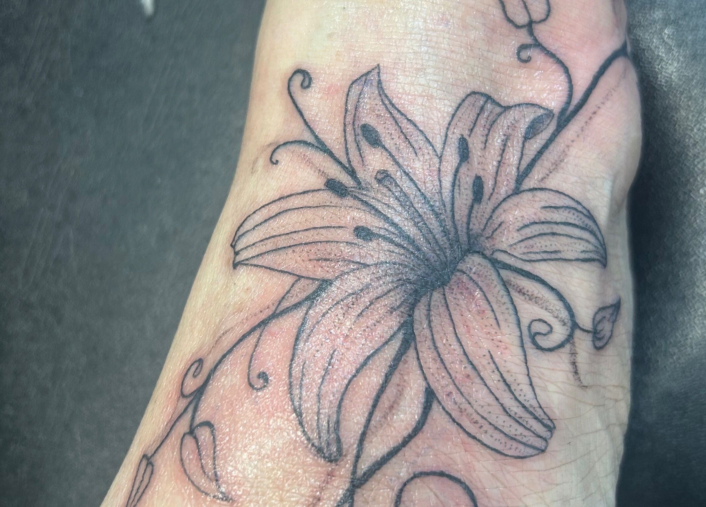 Detailed floral tattoo on foot at Navy, Halesworth, England, GB showcasing intricate line work.