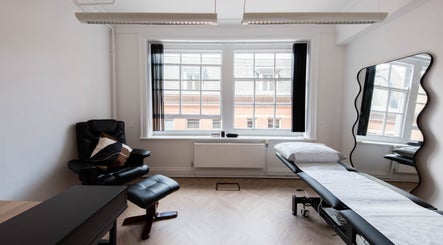 Relaxing treatment room at Soho Beauty & Aesthetics, London, England, GB, featuring a cozy chair and massage table.