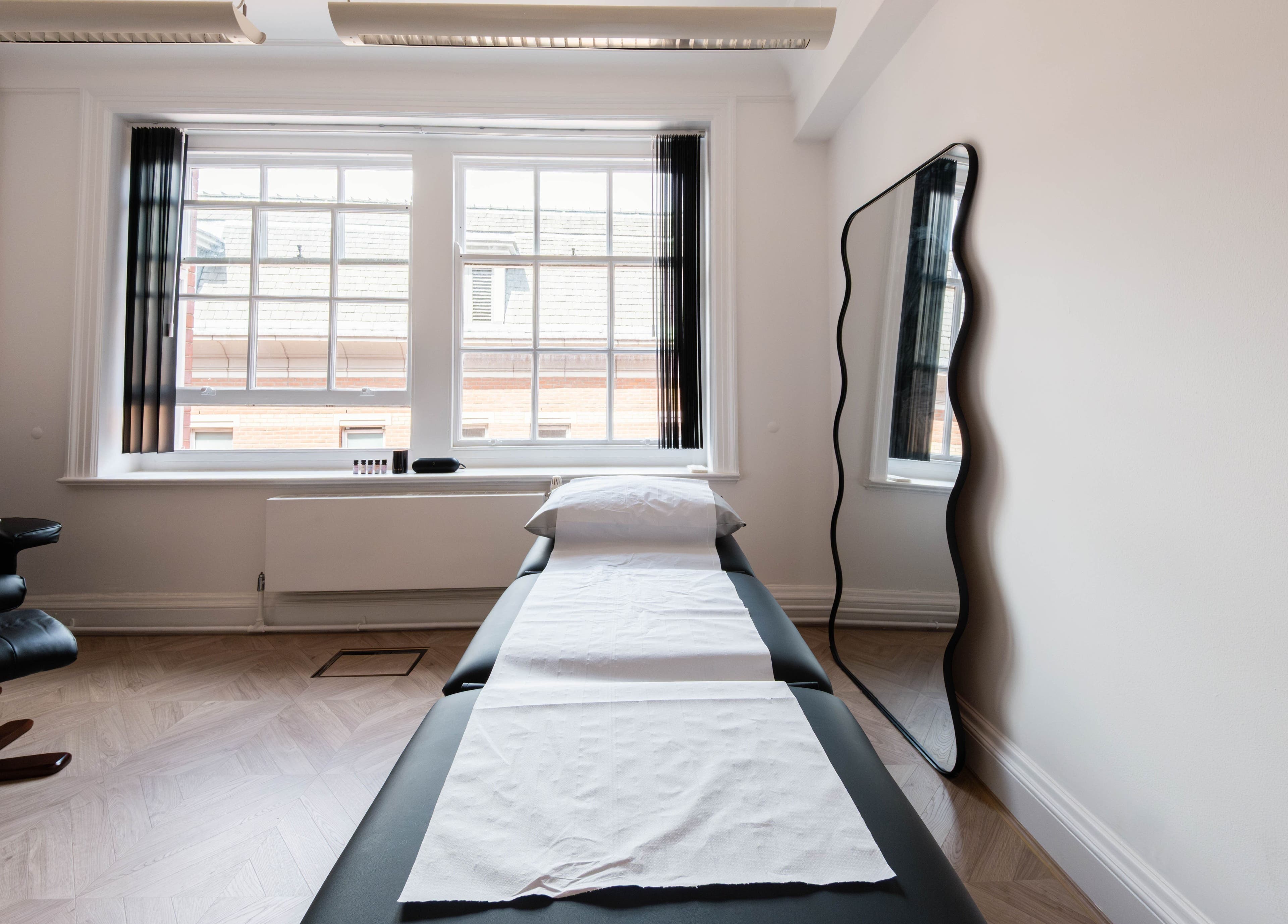 A tranquil treatment room at Soho Beauty & Aesthetics, London, England, GB, featuring a massage bed and natural light.