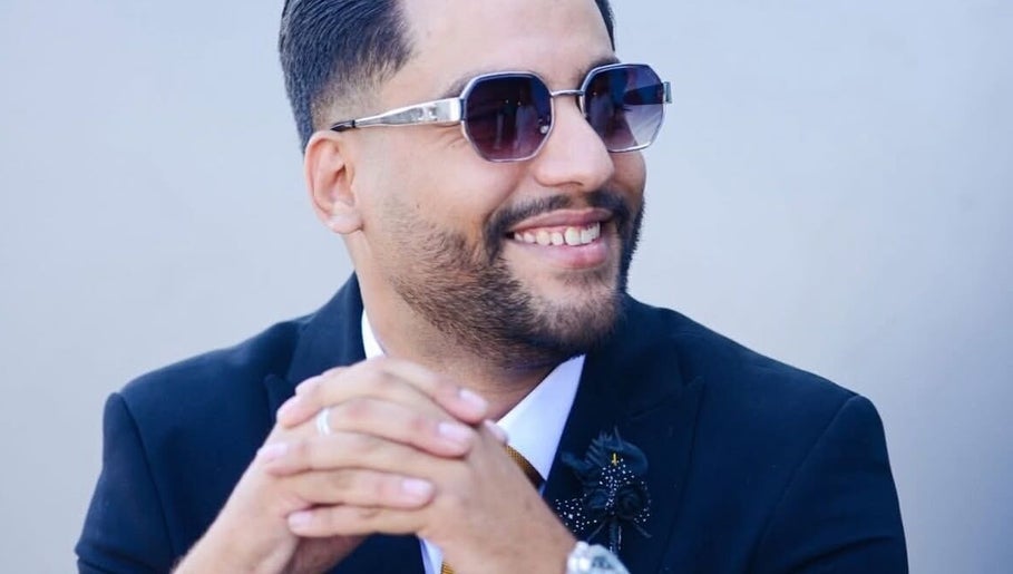 Confident individual at Nouh Barber, Dubai, AE wearing sunglasses and a suit with a smile.