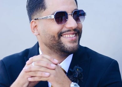 Confident individual at Nouh Barber, Dubai, AE wearing sunglasses and a suit with a smile.