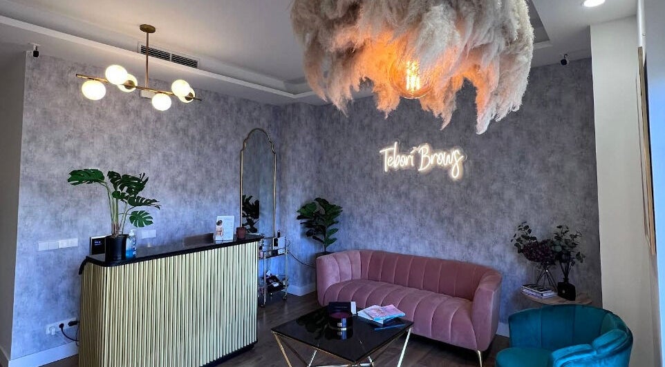 Recepción elegante en Teboribrows, Madrid, con sofá rosa y lámpara moderna.