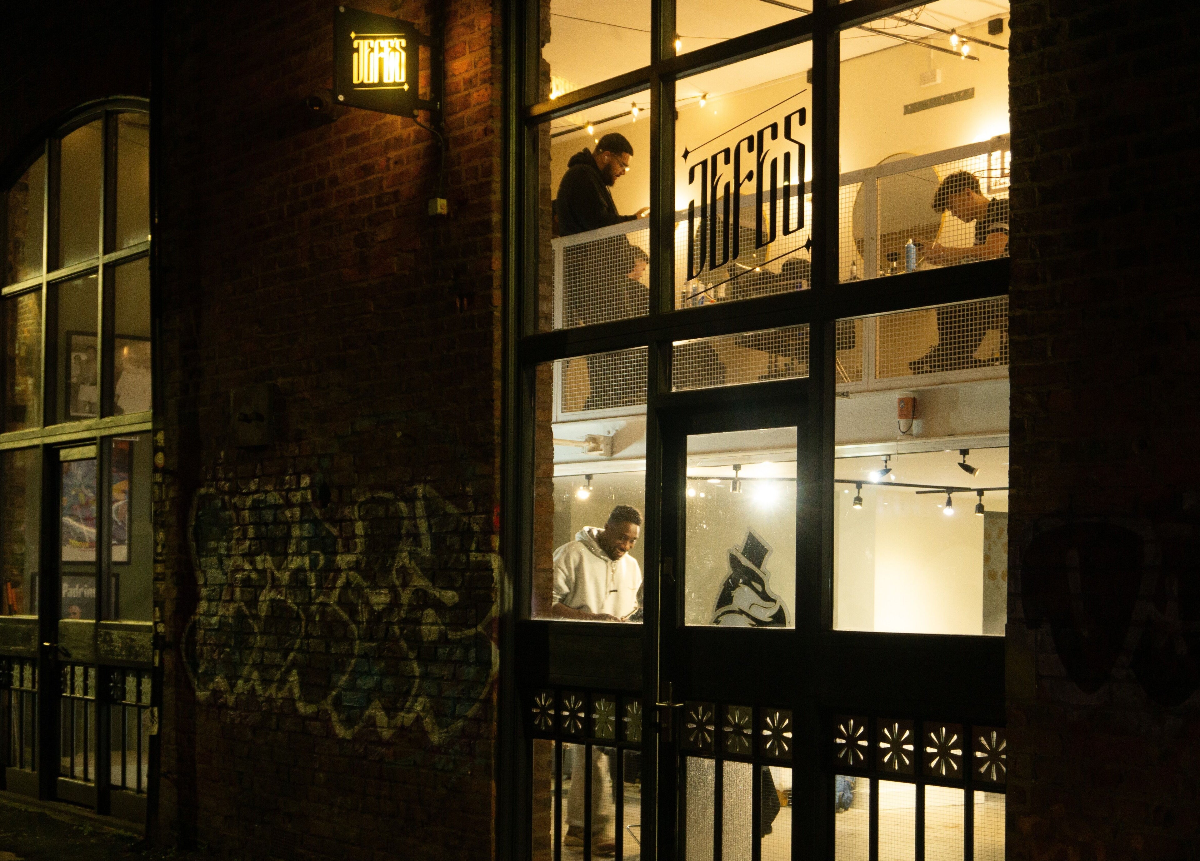 Exterior of Jefe's Barbers in Manchester, England, GB lit warmly at night, showcasing vibrant street scene.