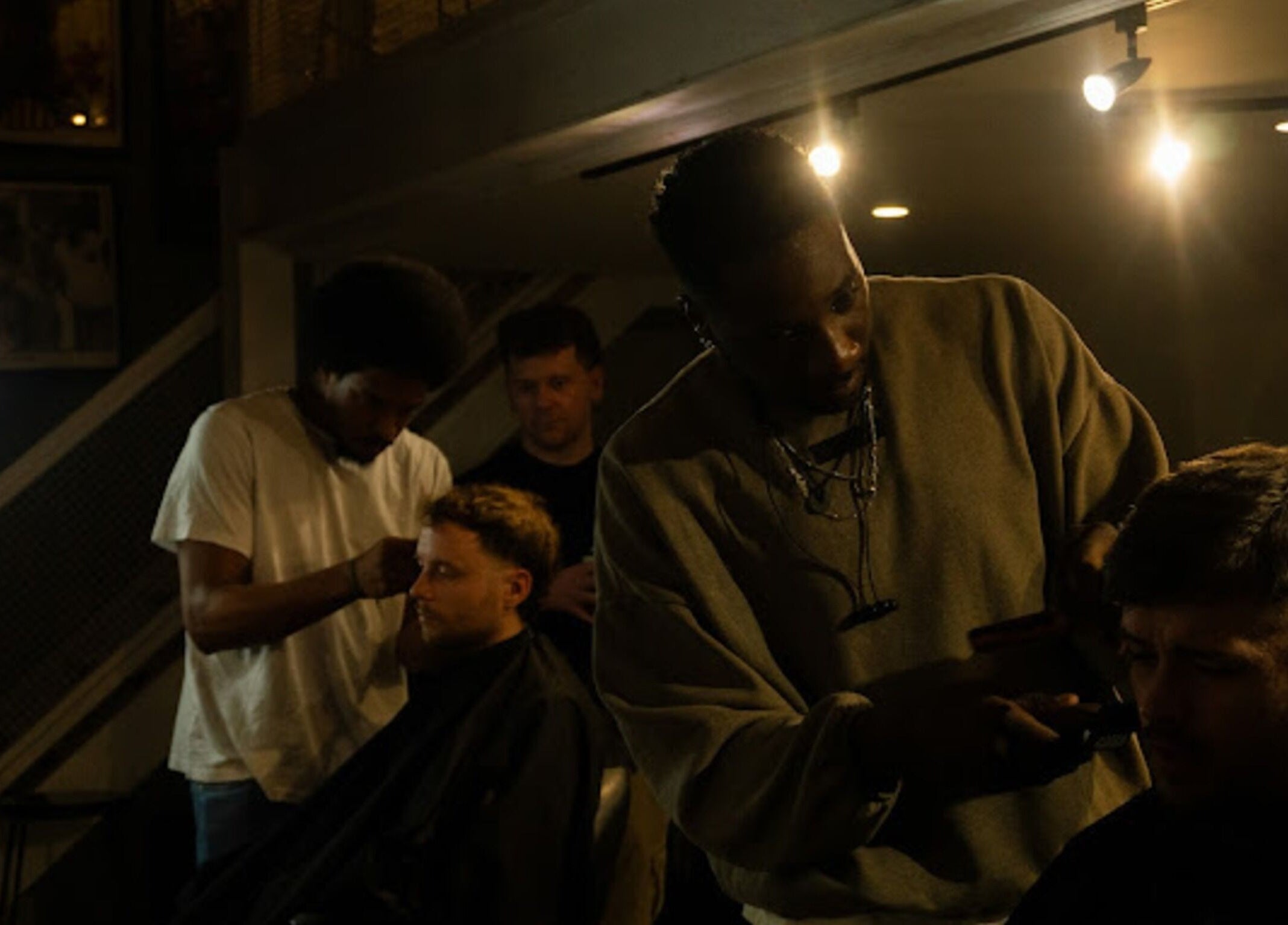 Barbers at work at Jefe's Barbers, Manchester, England, GB, under stylish lighting.
