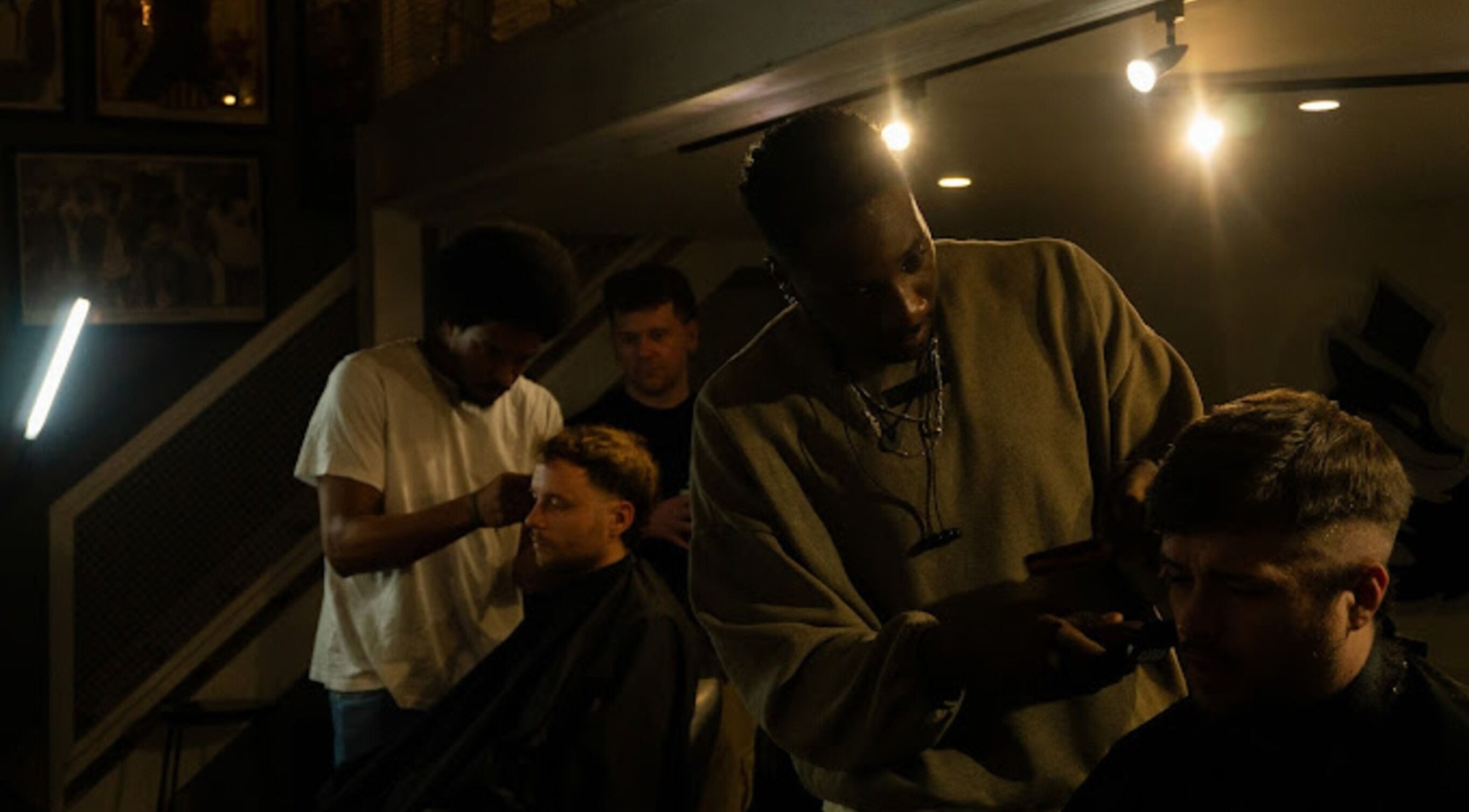 Barbers at work at Jefe's Barbers, Manchester, England, GB, under stylish lighting.