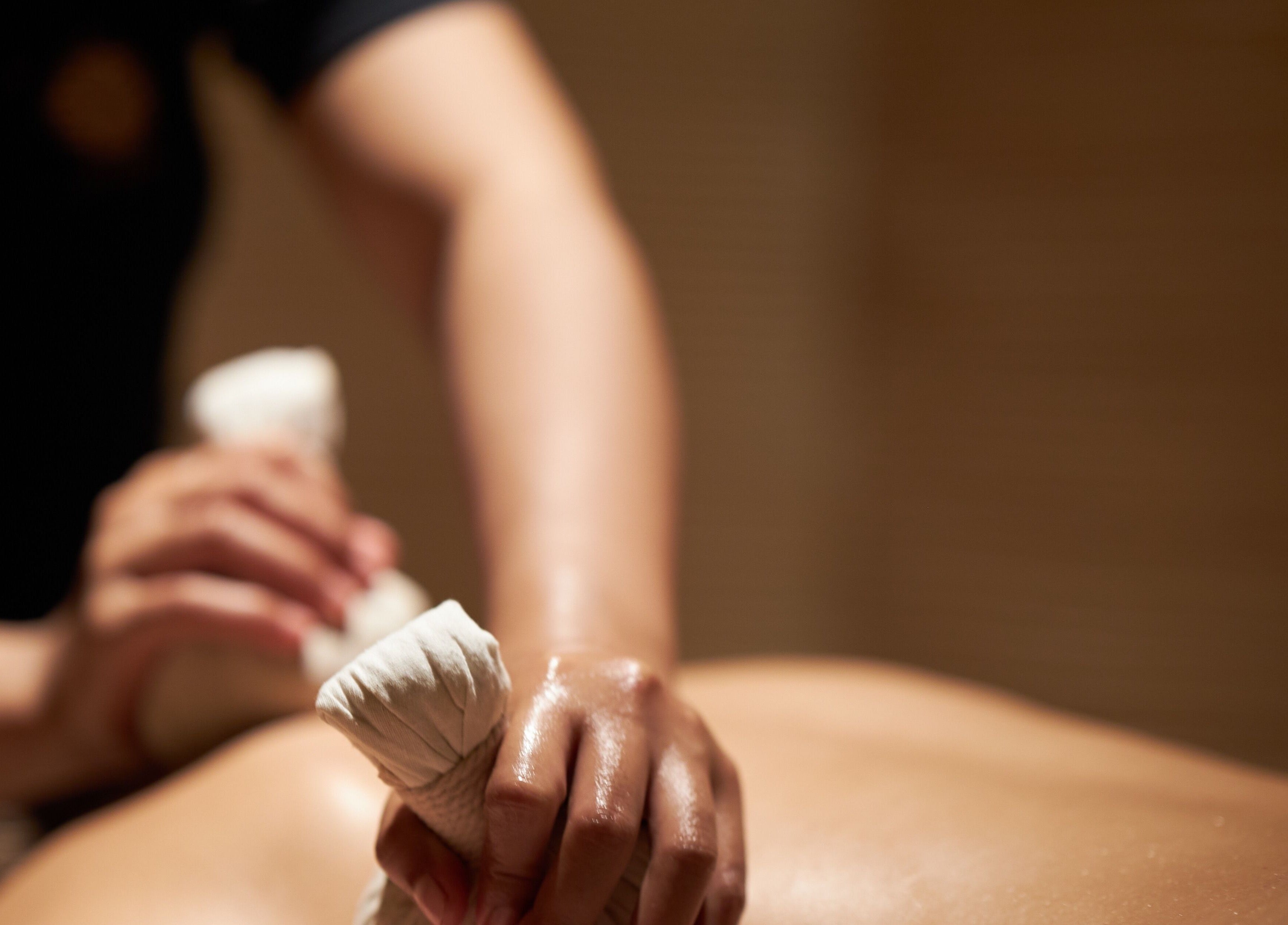 Therapist performing herbal compress massage at ATMOS BodyLab in Bali, Bali, ID for relaxation and wellness.