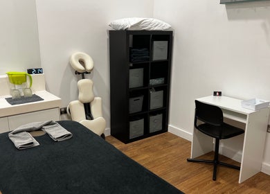 Cozy massage room at AR Sports Massage, London, England, GB with massage table, chair, and storage unit.