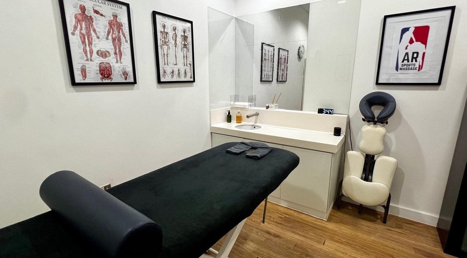 Therapy room at AR Sports Massage in London, England, GB, featuring massage table and anatomical posters.