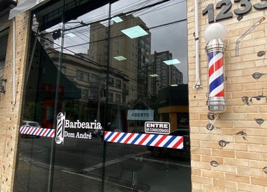 Entrada da Barbearia Dom André em São Paulo, SP com fachada de vidro e polo de barbearia clássico.