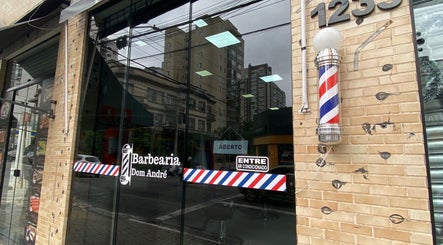 Entrada da Barbearia Dom André em São Paulo, SP com fachada de vidro e polo de barbearia clássico.