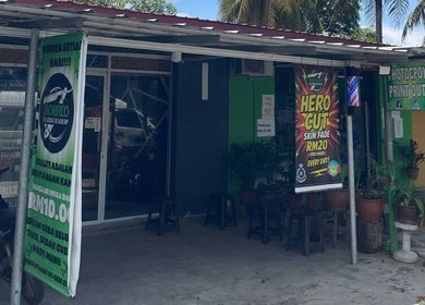 Street view of Borneo Barbershop Sabindo entrance in Penampang, Sabah, MY with vibrant banners and greenery.