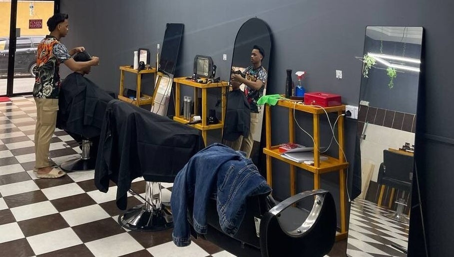 Inside Borneo Barbershop Putatan, Sabah, MY with barber attending to a customer on a stylish checkered floor.