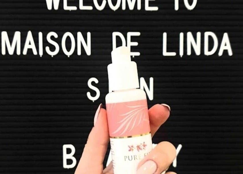 Hand holding skincare bottle in front of Maison de Linda Skin and Beauty sign, Richmond, Victoria, AU.