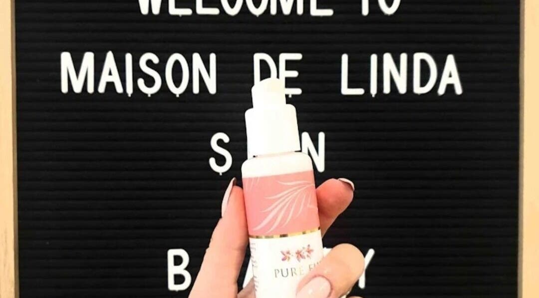 Hand holding skincare bottle in front of Maison de Linda Skin and Beauty sign, Richmond, Victoria, AU.