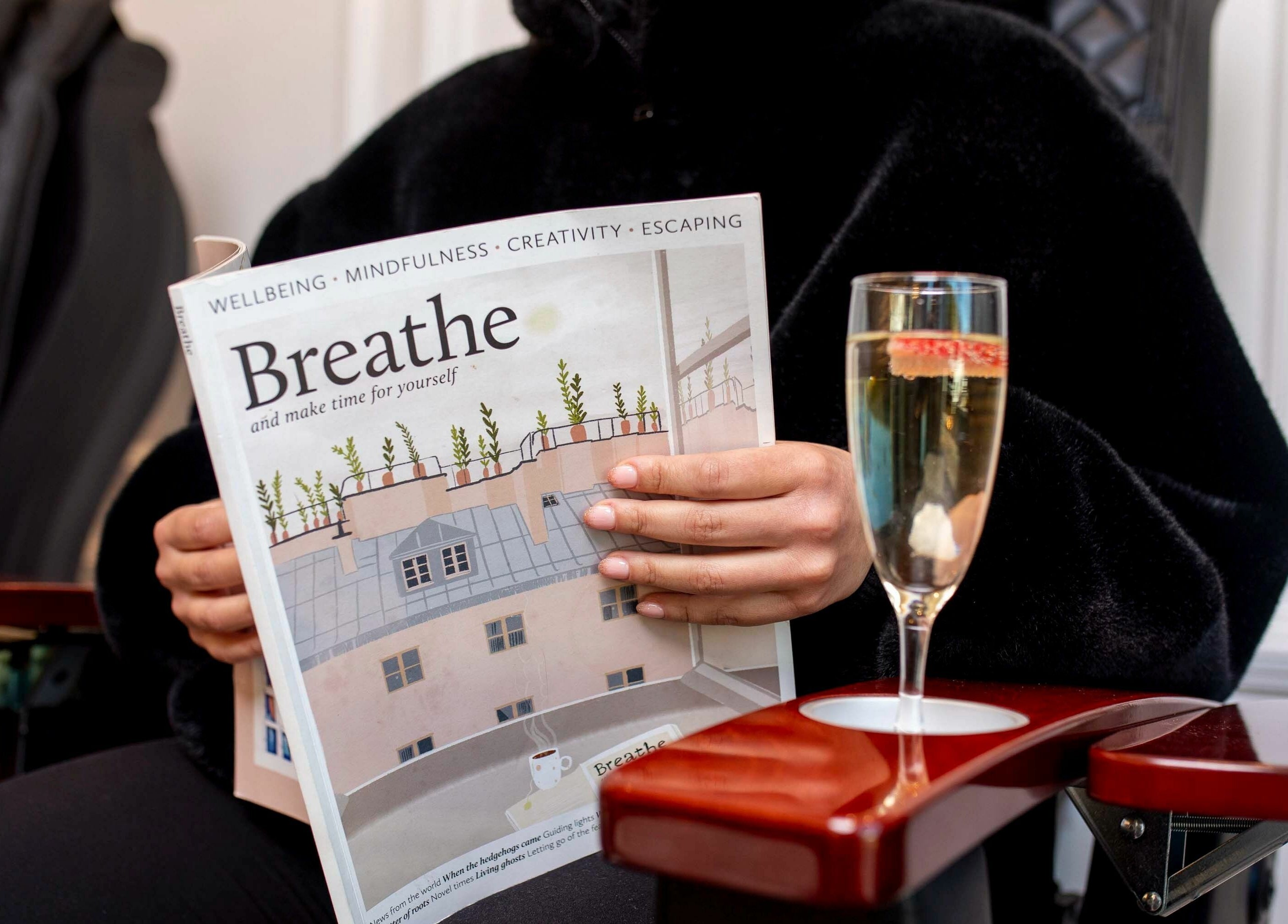 Person relaxing at Charm Clontarf, Dublin, holding a wellness magazine with champagne on a chair's armrest.