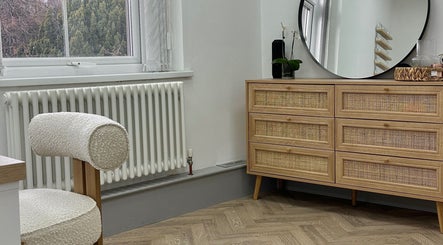 Elegant room at Mika Beauty, Wilmslow, England, GB, featuring a wood dresser, mirror, and cozy chair.