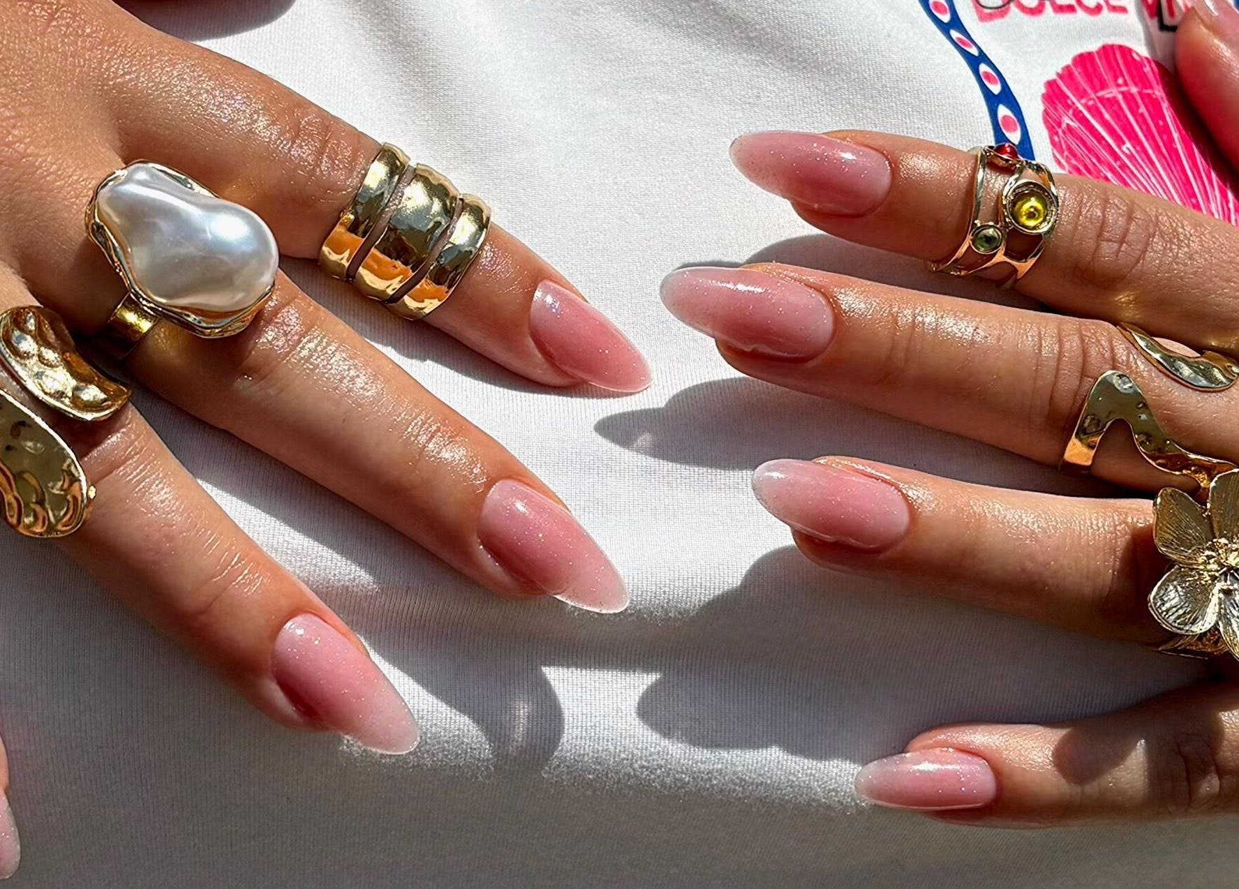 Mains avec manucure rose, bagues dorées chez Joy Nails, Niort, Nouvelle-Aquitaine, FR.