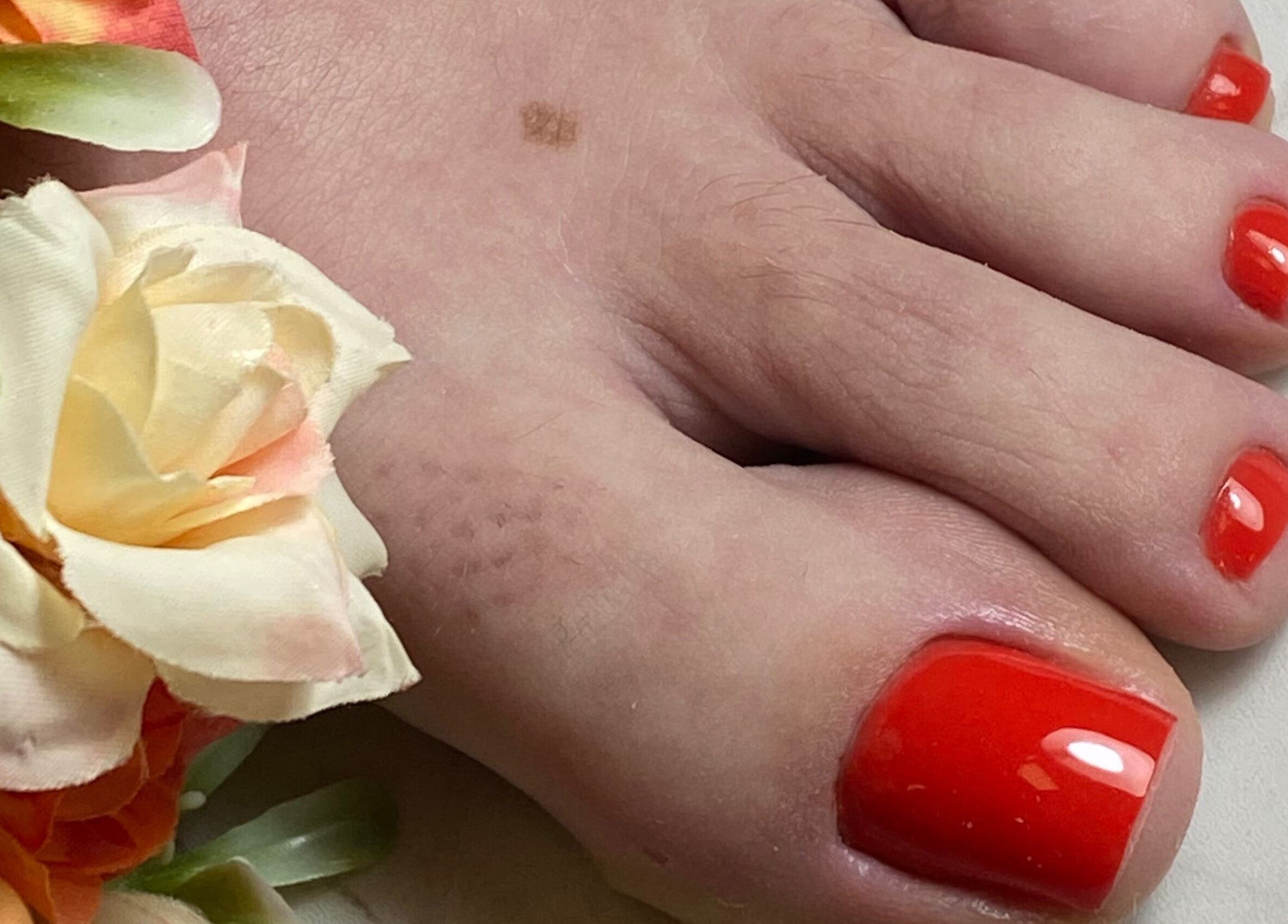 Pedicure vibrante em Studio Cuidar, Albufeira, Faro, PT, destacando unhas pintadas de vermelho e flores decorativas.