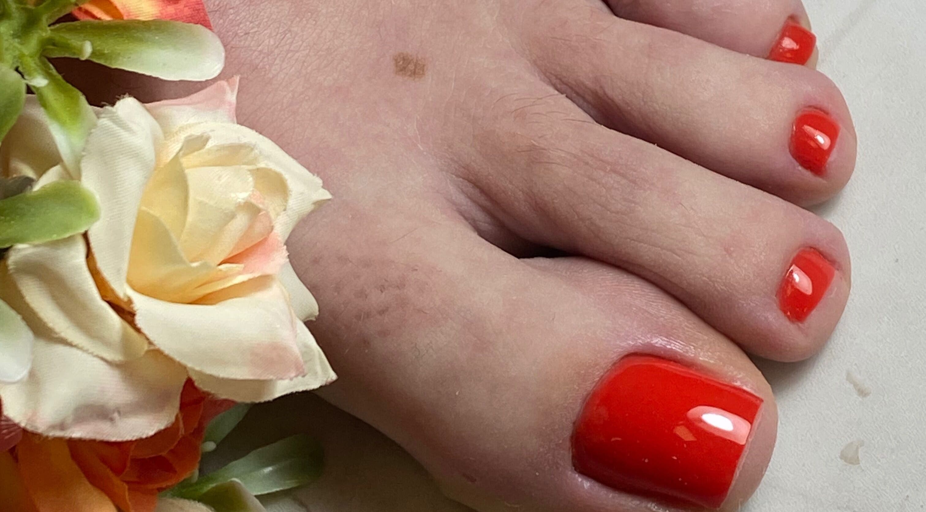 Pedicure vibrante em Studio Cuidar, Albufeira, Faro, PT, destacando unhas pintadas de vermelho e flores decorativas.