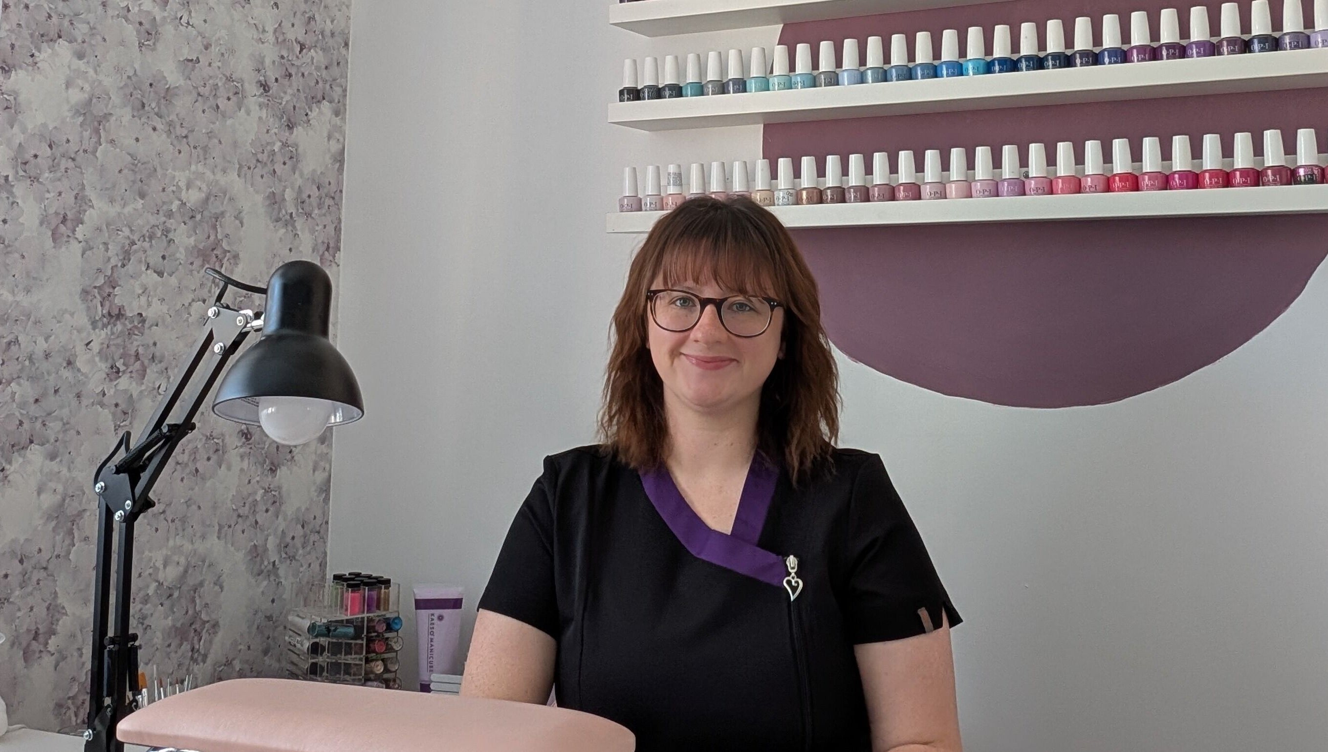Smiling professional at Peaceful Polish, Burry Port, Wales, GB, with nail polish display in the background.
