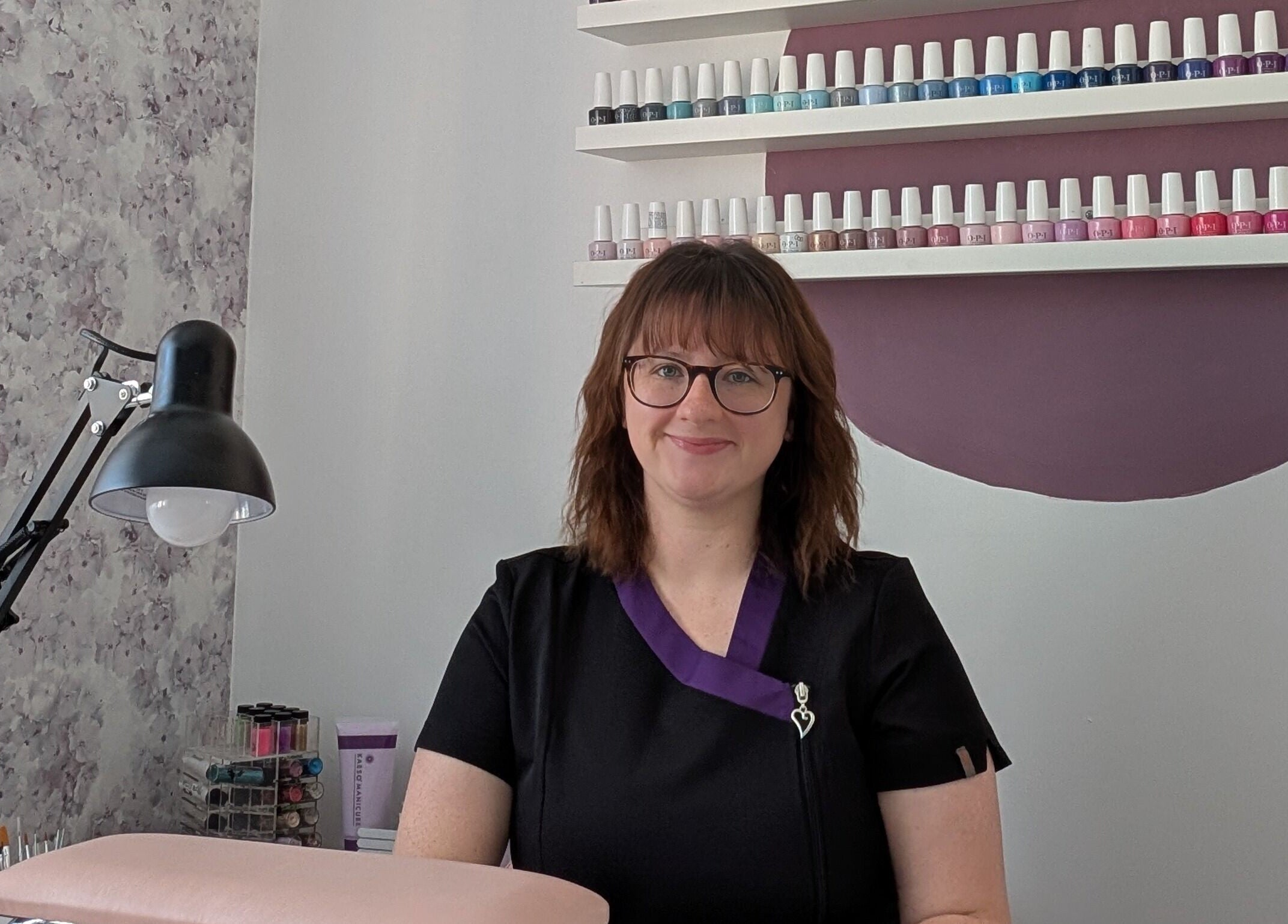Smiling professional at Peaceful Polish, Burry Port, Wales, GB, with nail polish display in the background.
