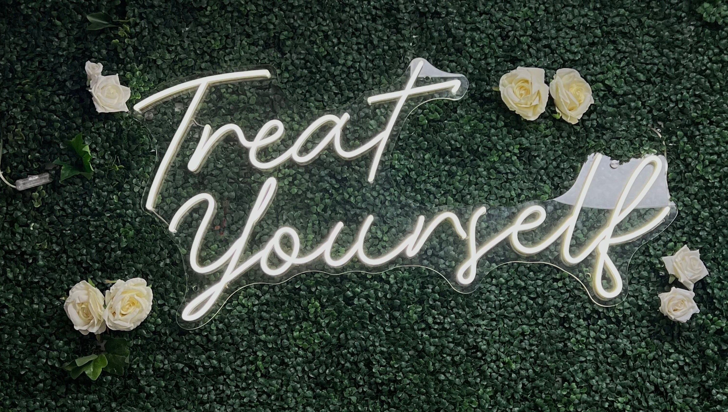 Neon 'Treat Yourself' sign at Illuminate Aesthetics Lounge, Toronto, Ontario, CA, on a lush green backdrop.