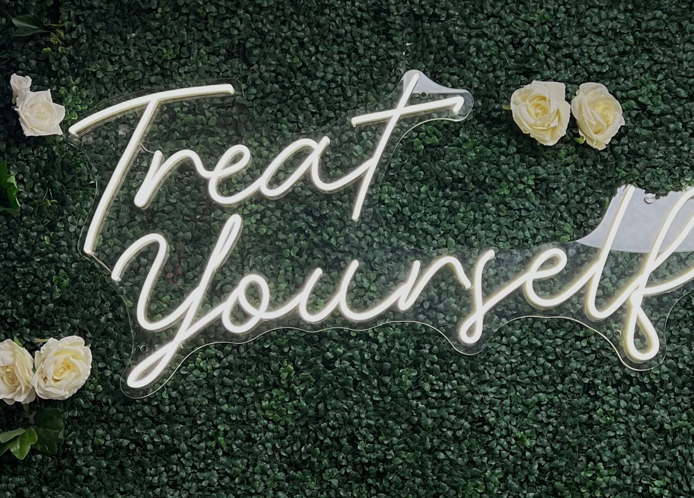 Neon 'Treat Yourself' sign at Illuminate Aesthetics Lounge, Toronto, Ontario, CA, on a lush green backdrop.
