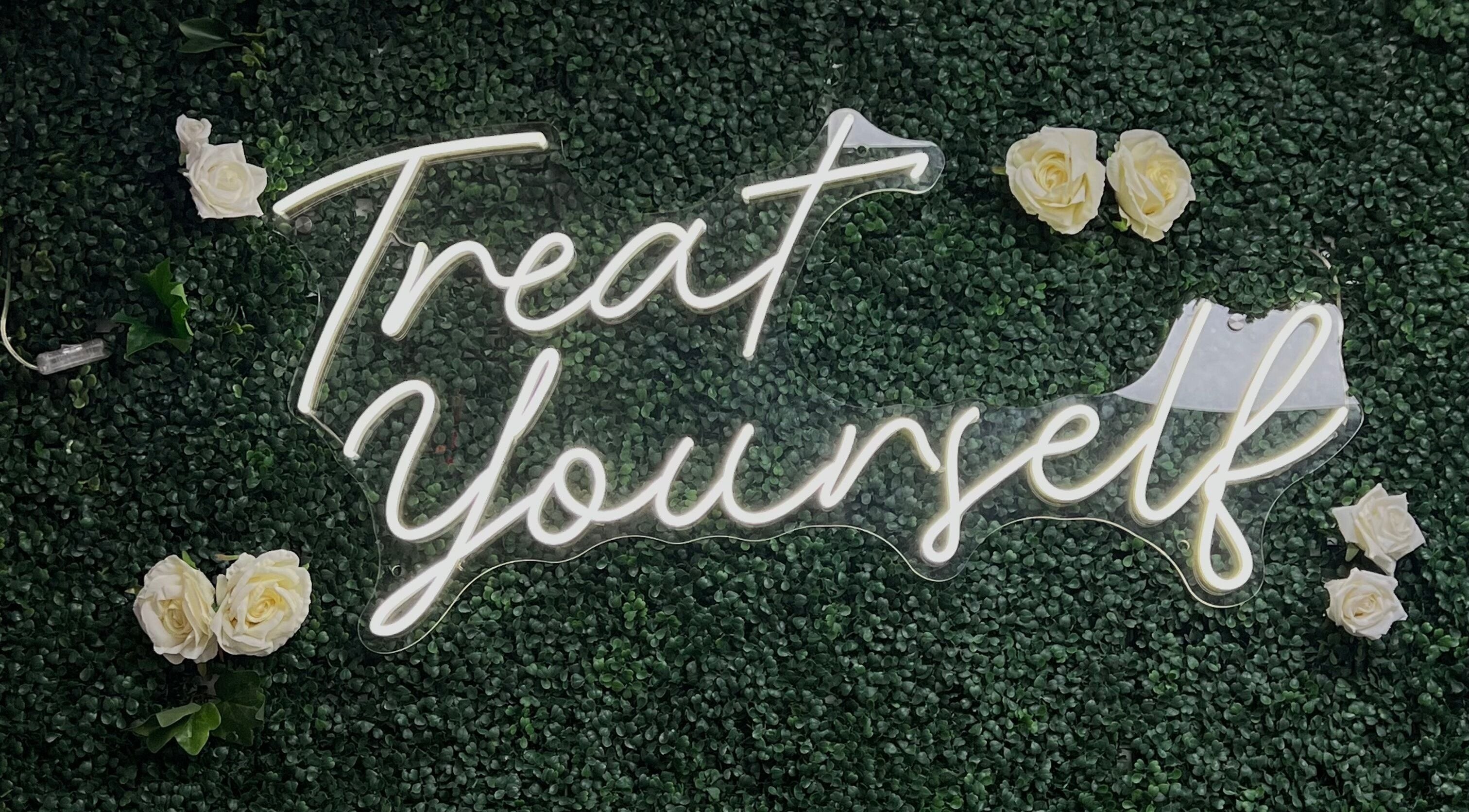 Neon 'Treat Yourself' sign at Illuminate Aesthetics Lounge, Toronto, Ontario, CA, on a lush green backdrop.