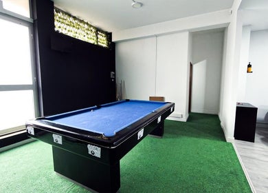 Sala de lazer em Barbearia Maia, Braga, PT, com mesa de bilhar e cadeiras de barbeiro modernas.