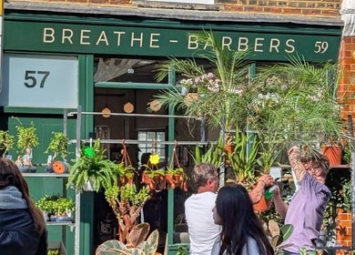Exterior view of Breathe Barbers in London, England, GB with lush plants and people outside.