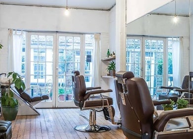 Bright and spacious barber area at Breathe Barbers, London, England, GB with stylish chairs and plants.