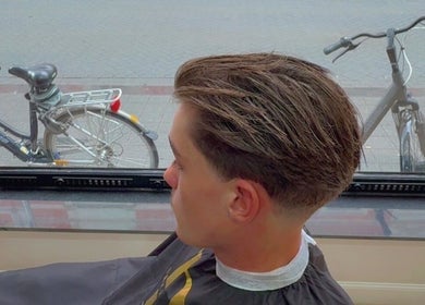 Trendy kapsel bij Dakhil kapper, Turnhout, Vlaams Gewest, BE. Jonge man met gestileerd haar vanuit raamzicht.