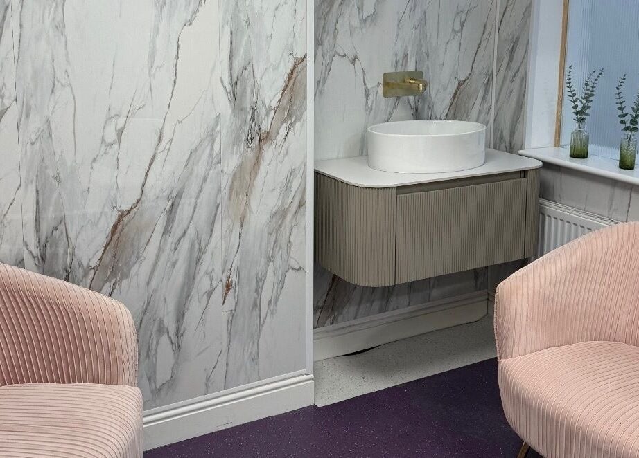 Chic waiting area with pink chairs at Clinic 103, Harpenden, England, GB featuring a marble wall.