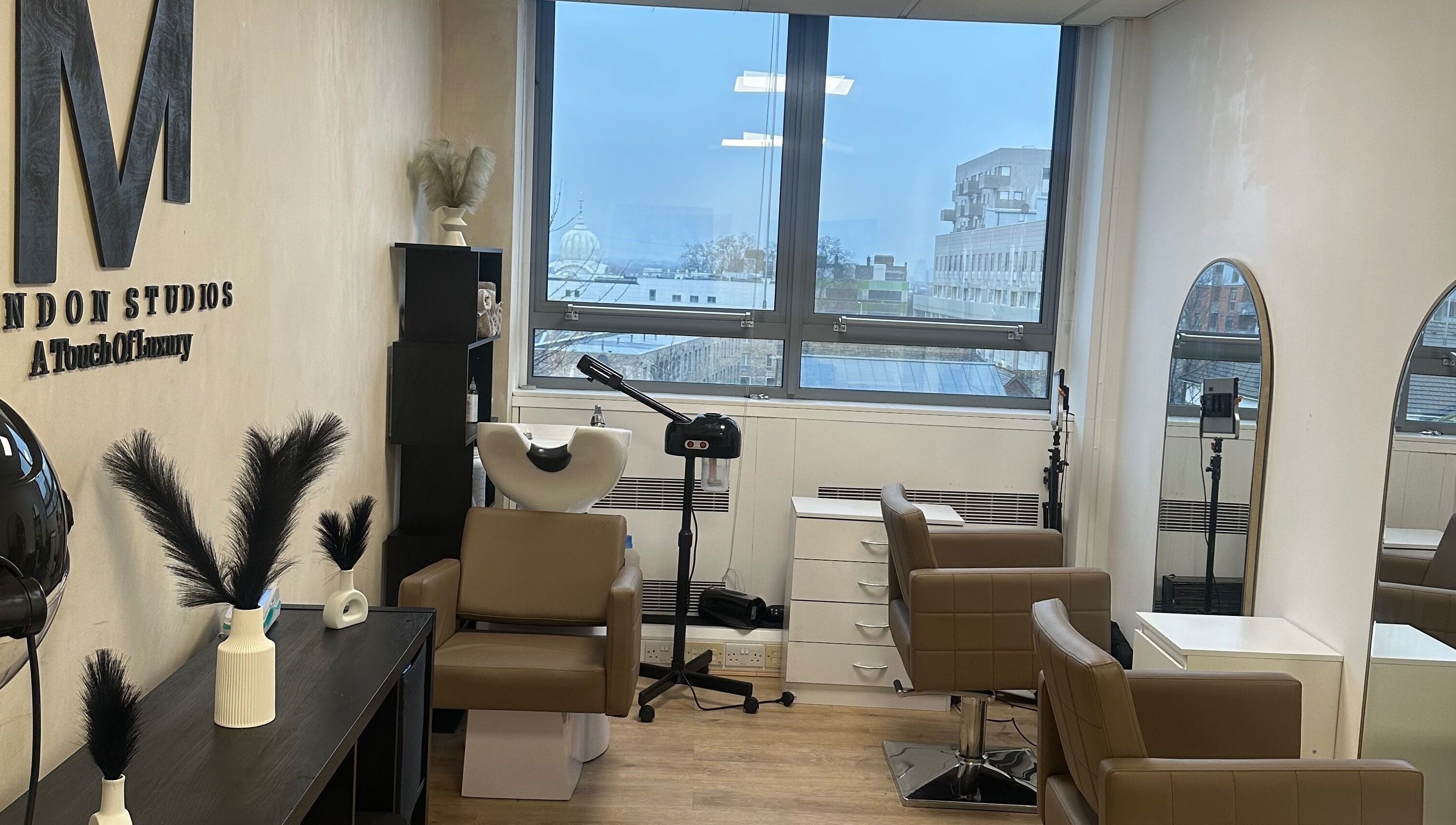 M London Studios in Barking, England, GB. Modern beauty setup with chairs, mirrors, and large window view.